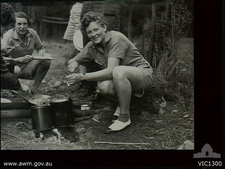 A WAAAF officer trainee prepares a meal over an open fire